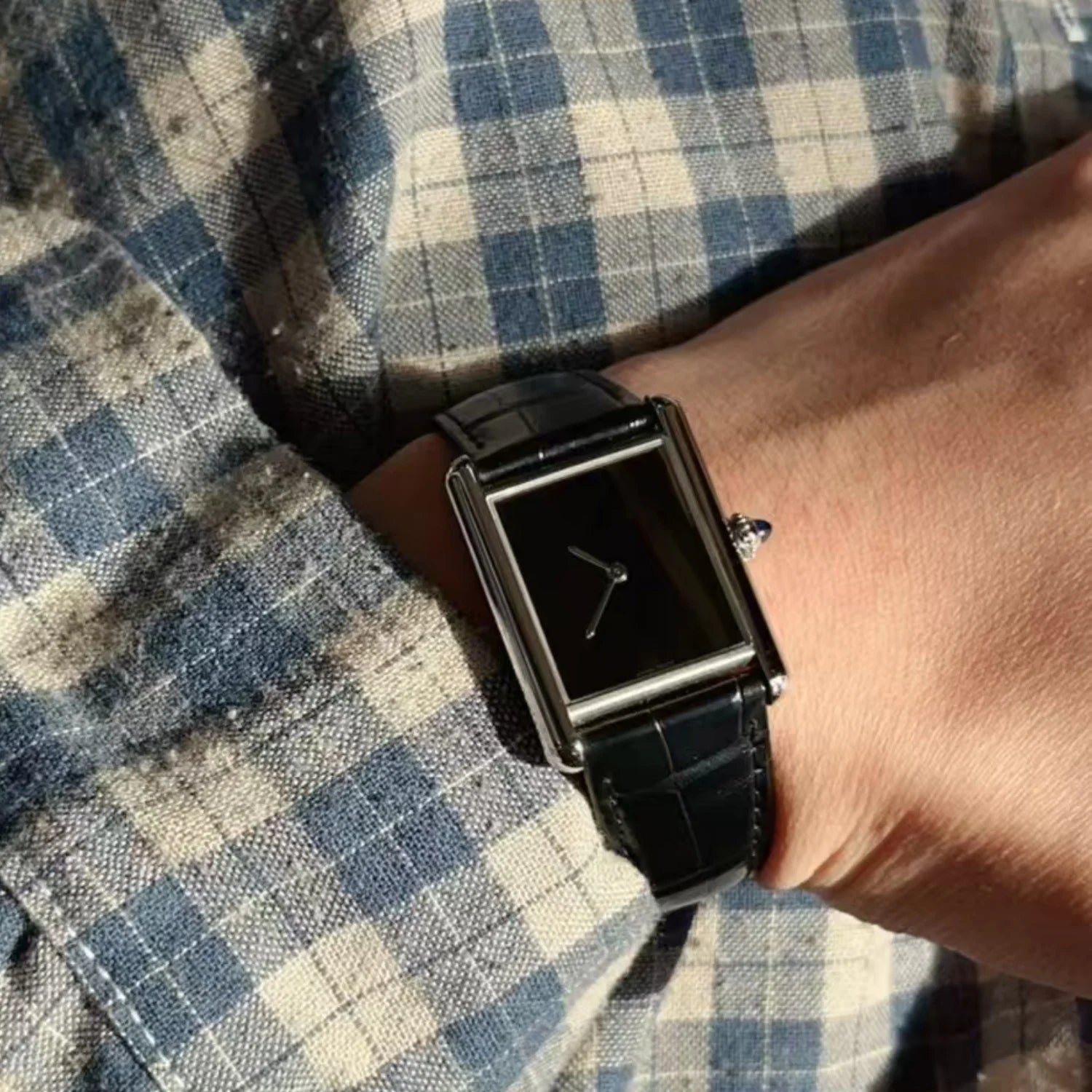 A man wearing a blue plaid flannel shirt showing the black leather strap variant of the CILOA minimalist square tank watch on his wrist
