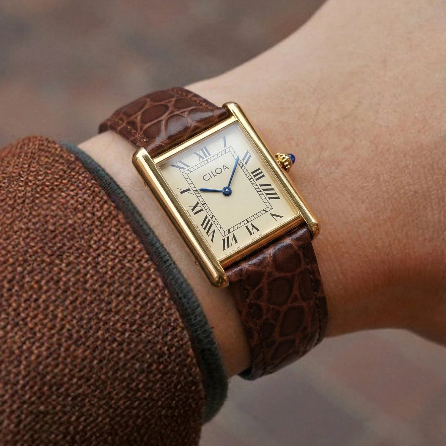 Side view of a man's wrist wearing the gold CILOA square tank watch with a cream face, paired with a textured brown knit sweater