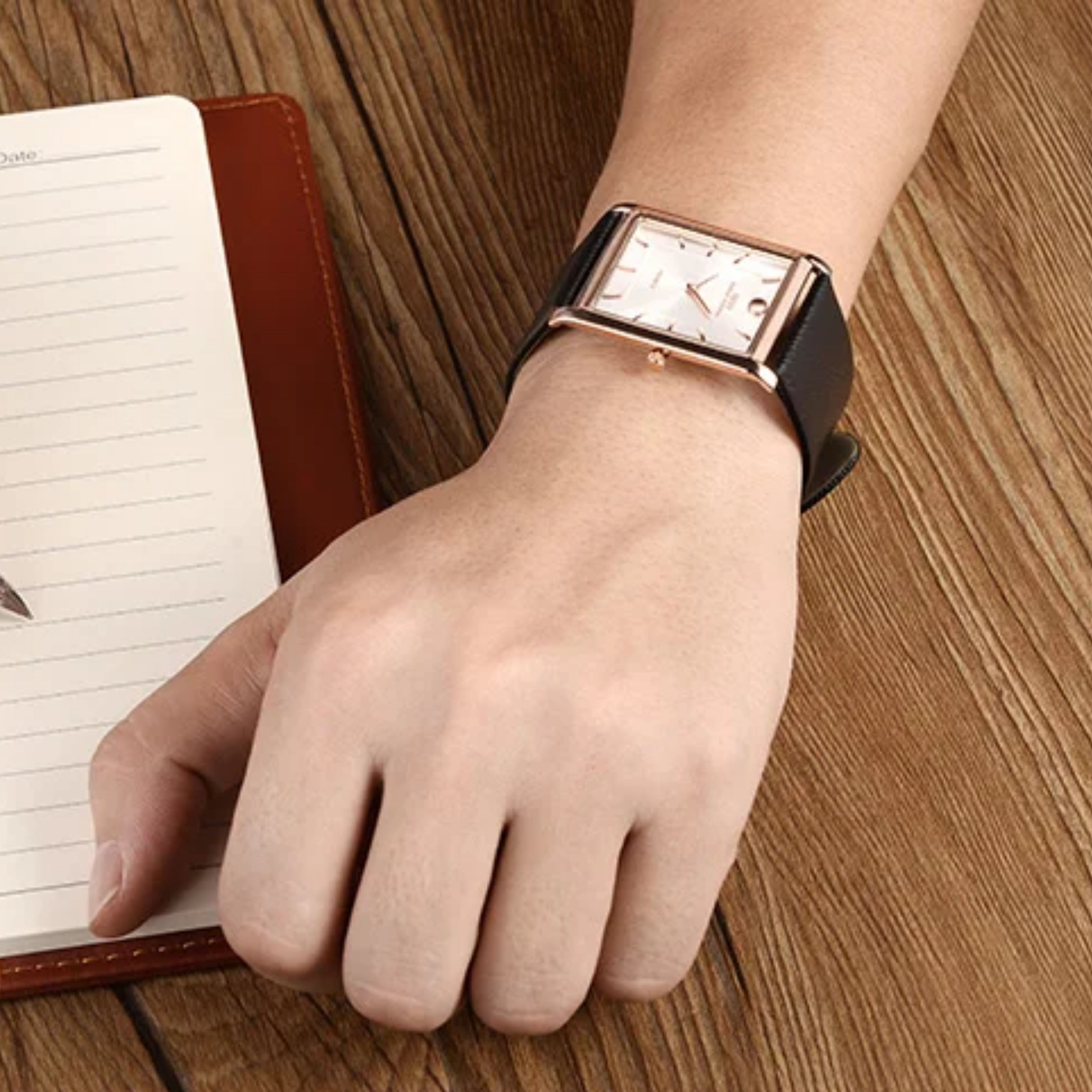 Close-up of a man's wrist wearing the IBSO rose gold rectangular watch with a white dial, styled next to an executive desk planner