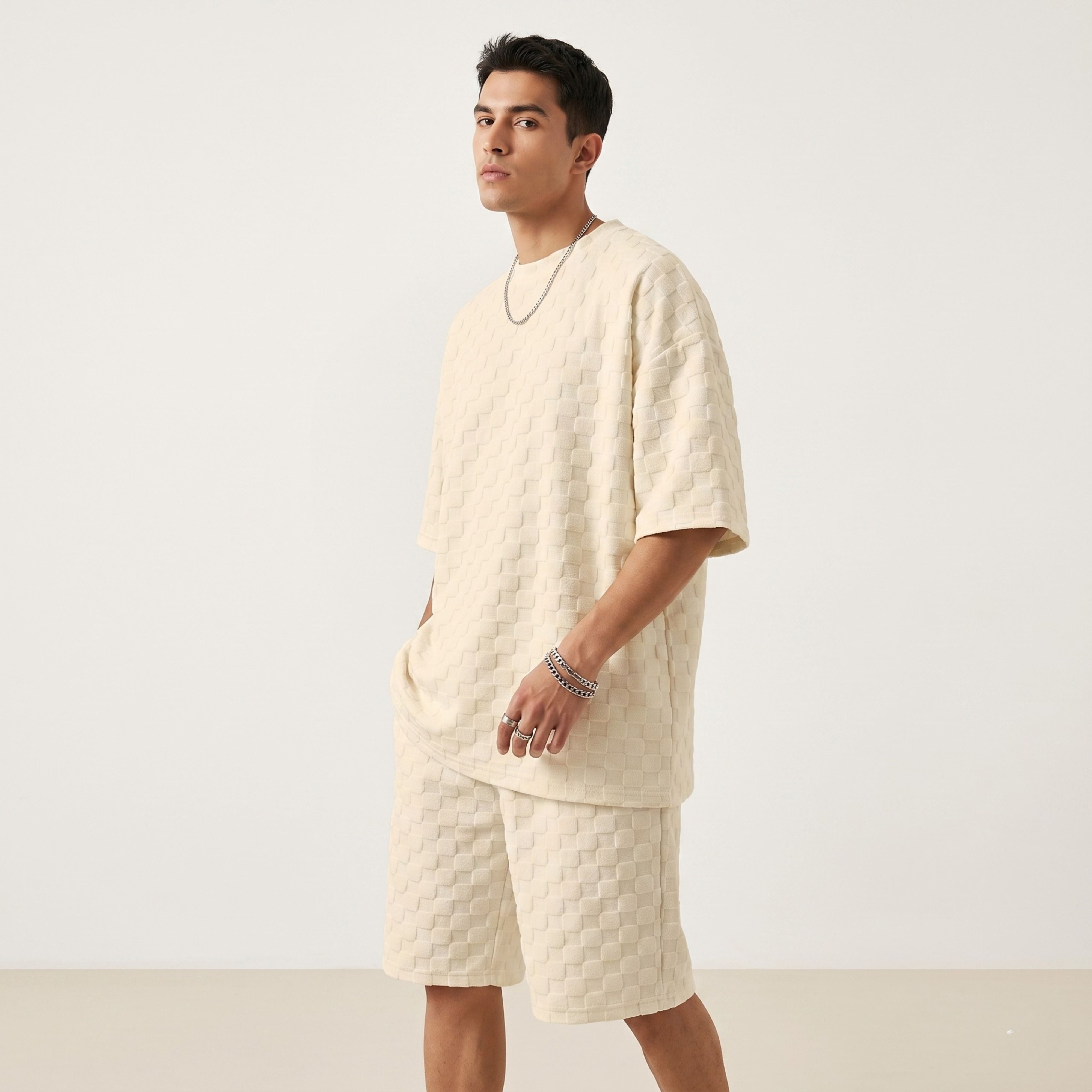 Full body shot of a male model wearing the loose-fit beige jacquard plaid short-sleeve T-shirt and matching drawstring casual shorts