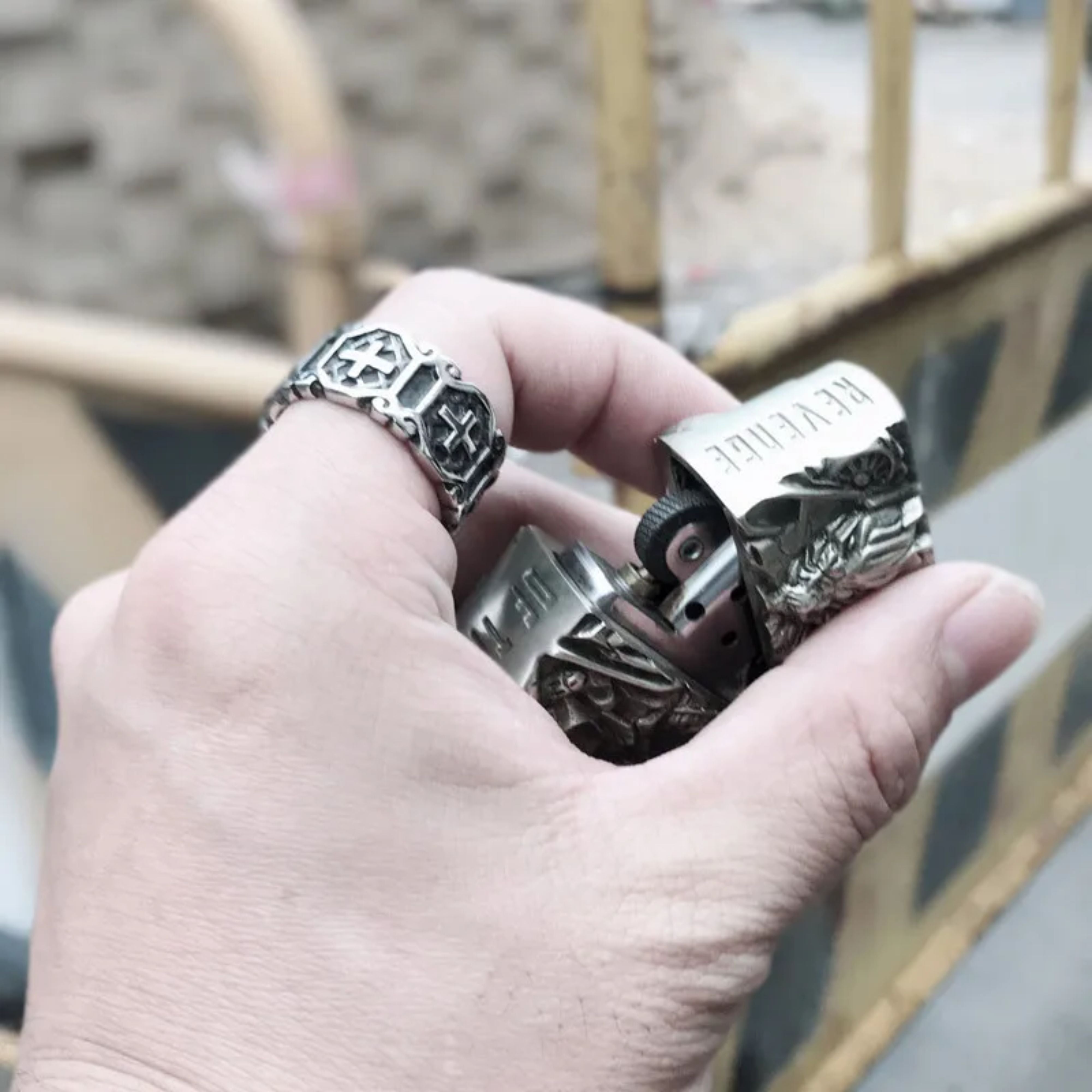 Lifestyle shot of a man's hand wearing the vintage silver cross biker ring outdoors with a blurred urban background.