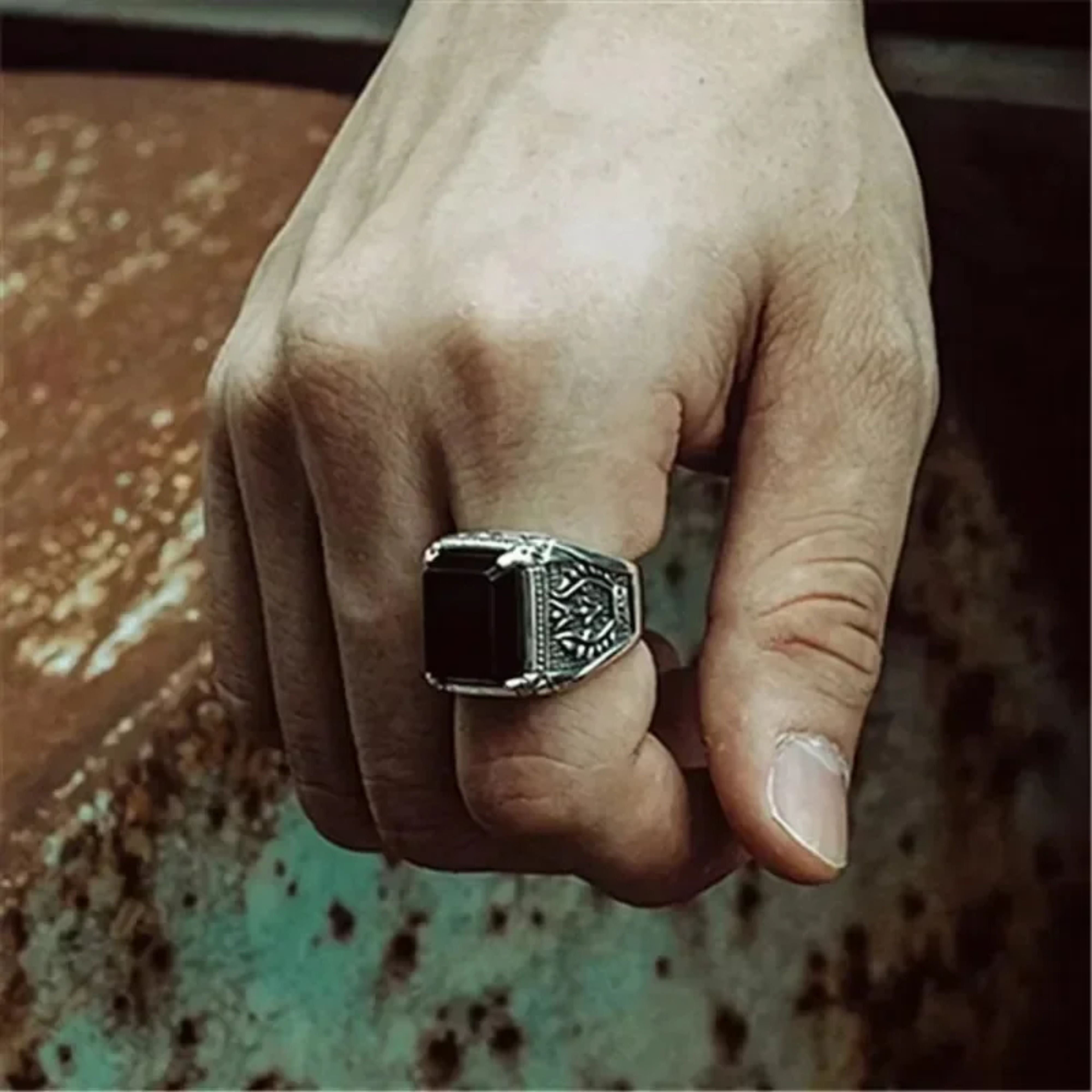 Men's vintage silver ring with a large red stone worn on a hand against a rustic metallic background.
