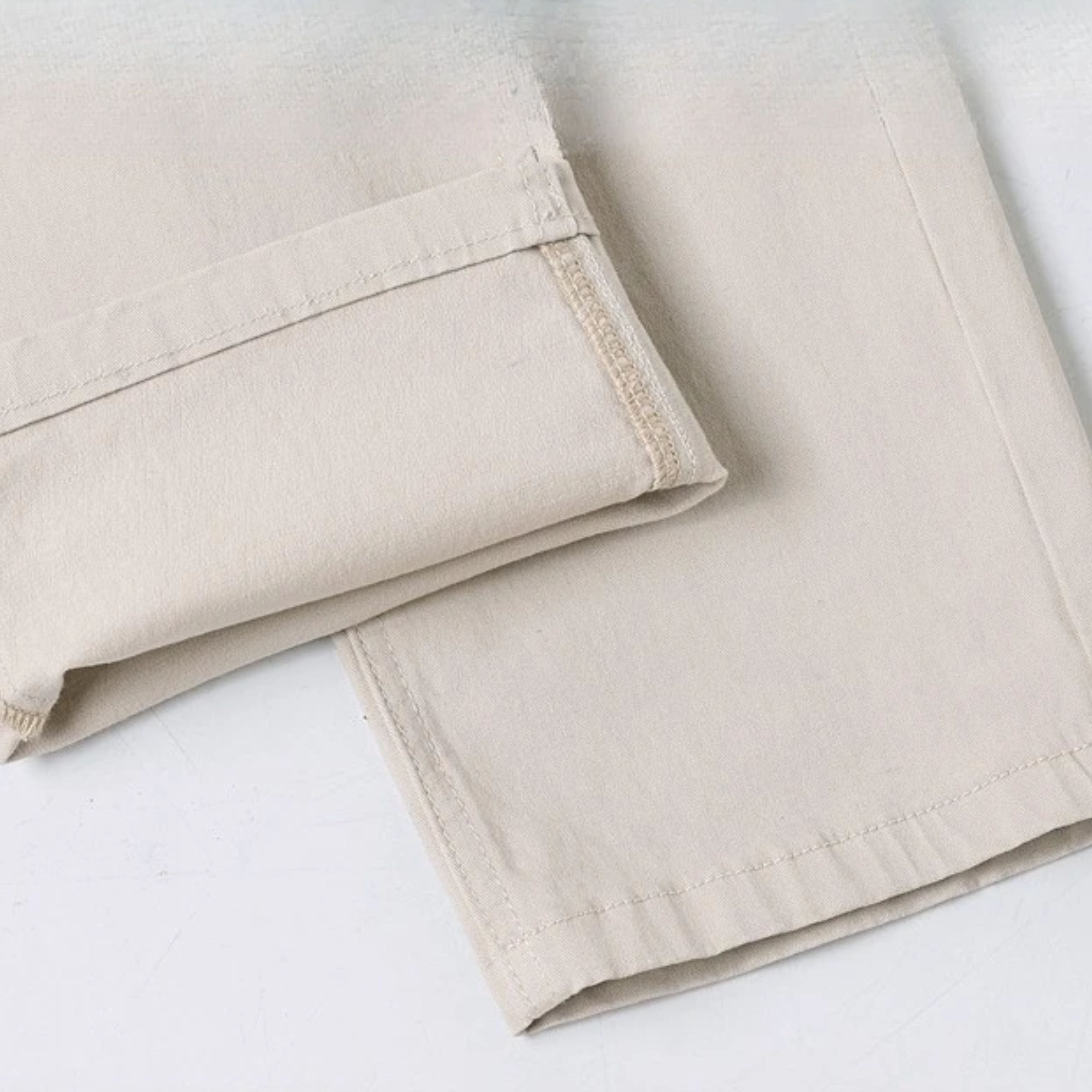 Close-up shot of the turned-up straight ankle hem on the off-white stretch denim, showcasing the clean dual-thread interior stitching lines