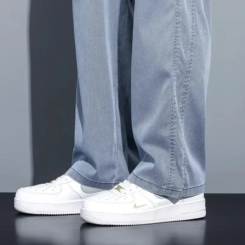 Detailed lower leg view showing the fluid straight drape hemline of light blue men's casual trousers resting over clean white leather sneakers
