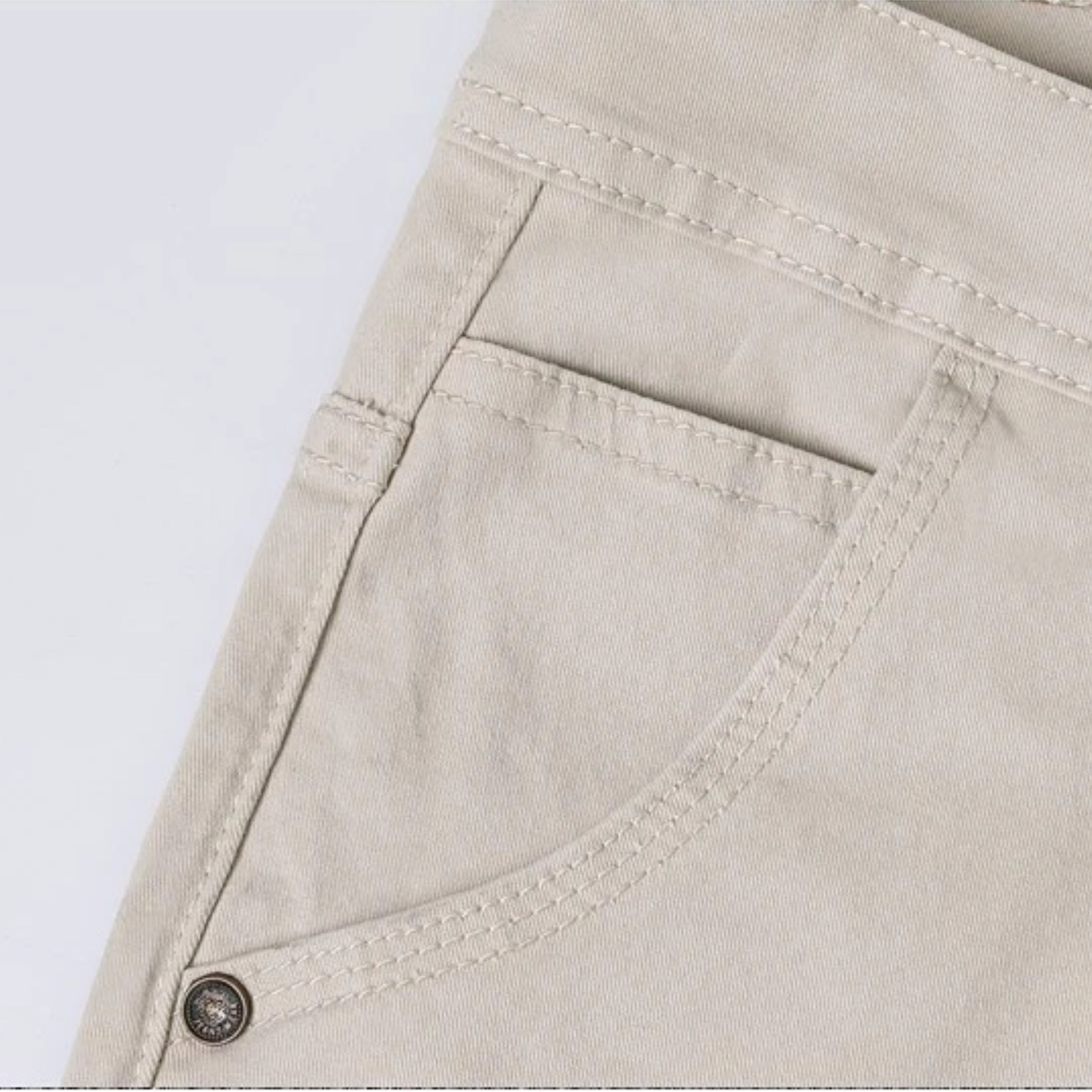 Close-up display of the sleek front pocket construction on the sand beige denim pants, showing the clean watch pocket and metallic accent rivet