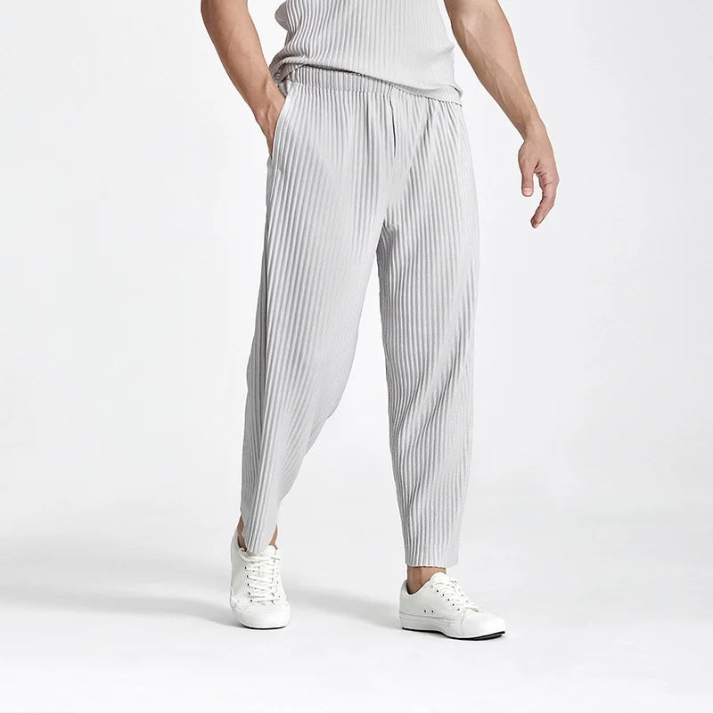 Model wearing men's gray pleated straight-leg pants paired with white sneakers for a casual summer outfit