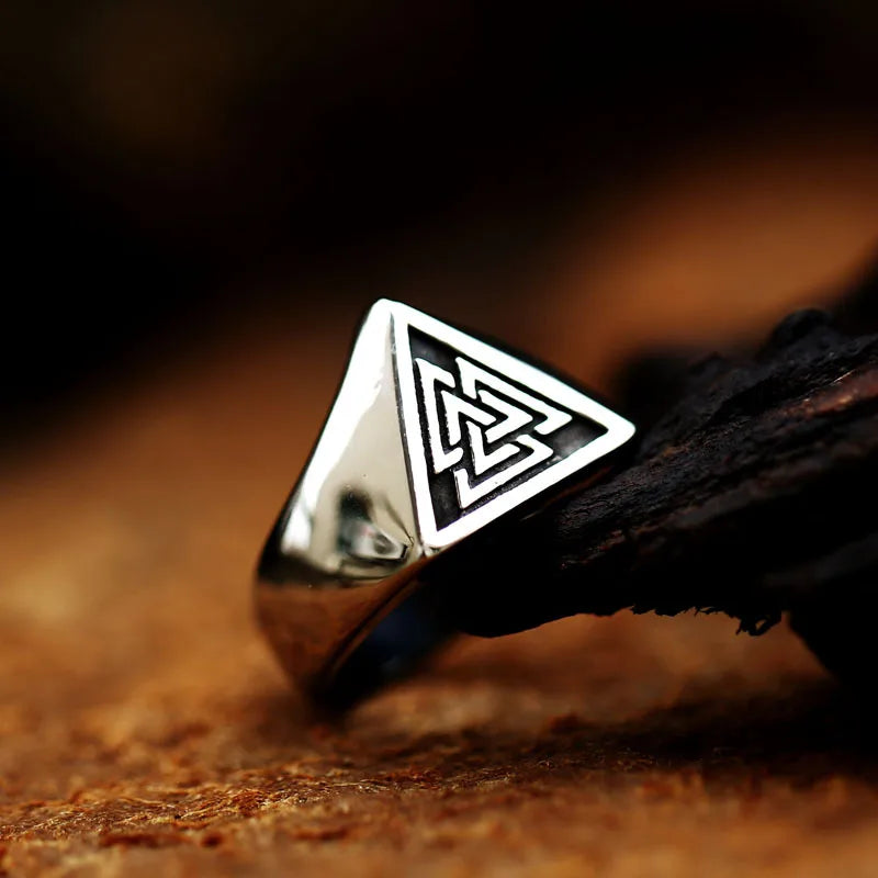 Macro shot of an oxidized silver Viking Valknut ring resting on dark wood, showing the triangular face details.