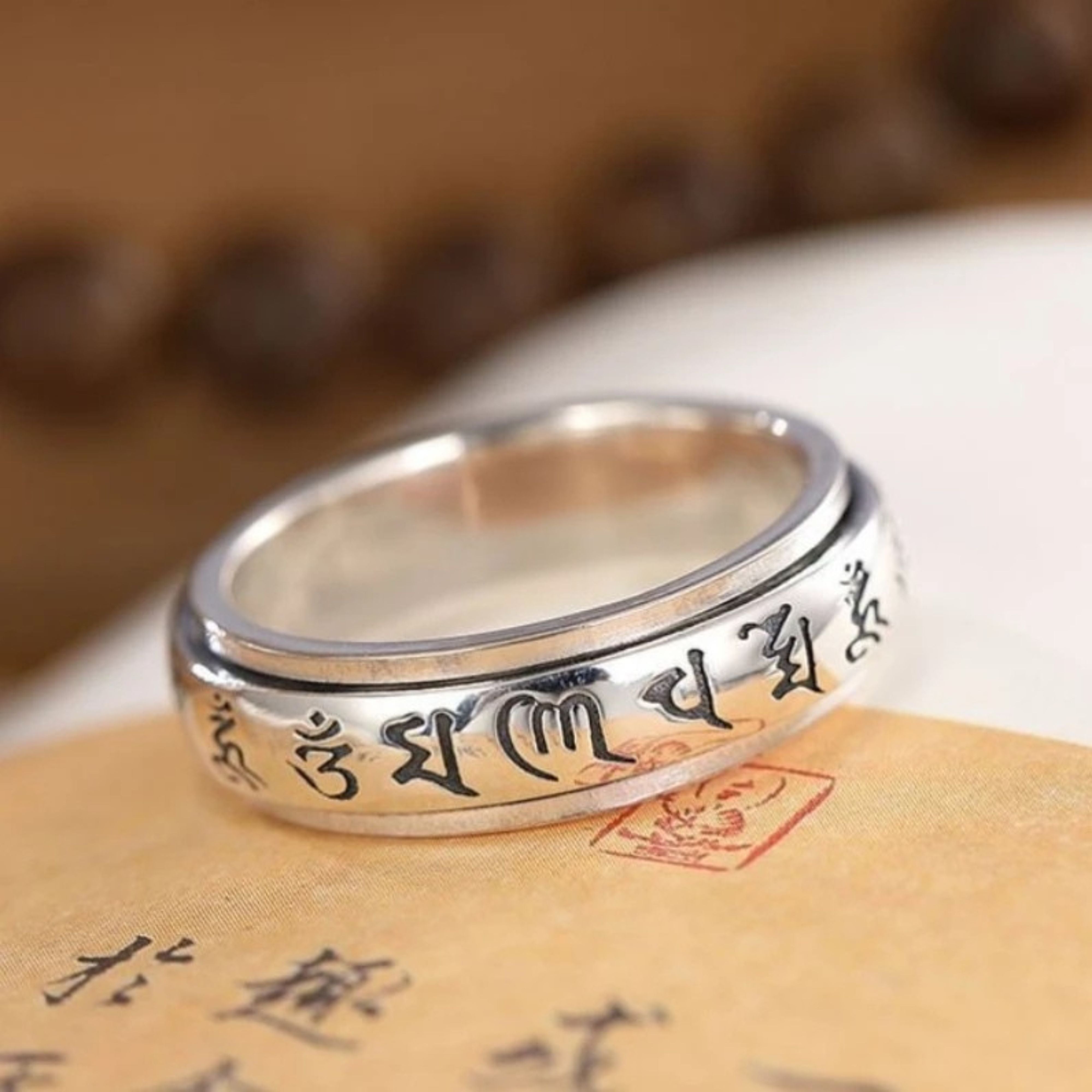 Silver Tibetan mantra spinner ring resting flat on vintage calligraphy paper with traditional red ink stamps.