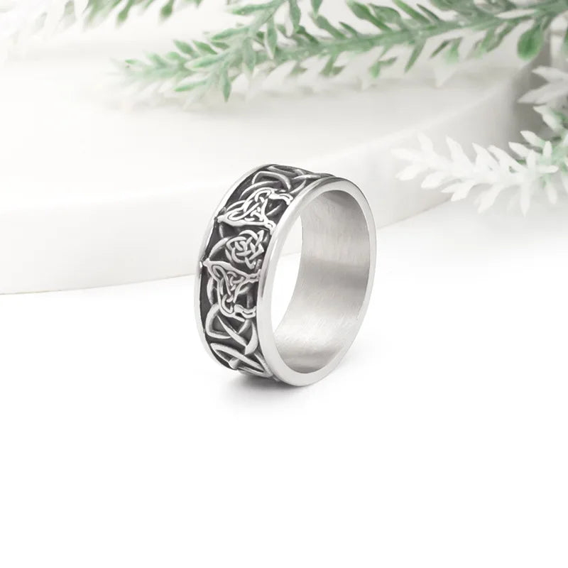 Silver Norse mythology wolf ring standing upright next to green foliage on a white surface.