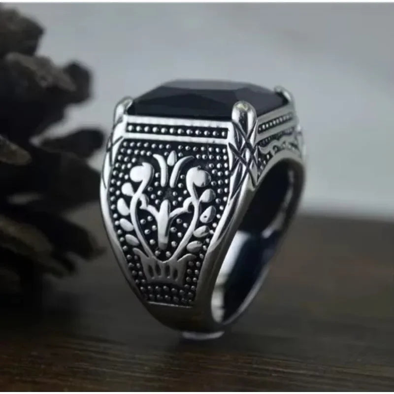 Chunky men's silver ring with a large black rectangular stone standing upright on a dark wooden surface.