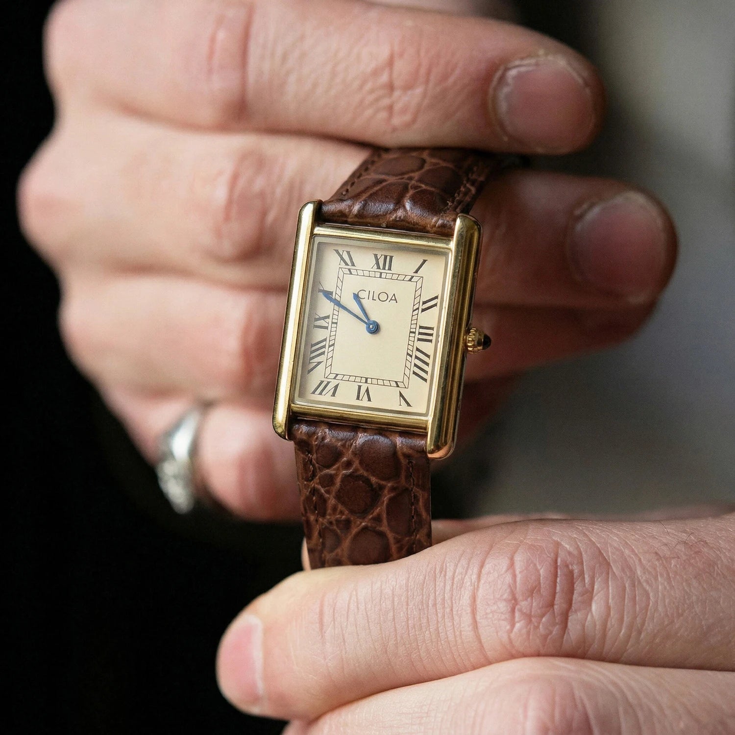 A person holding the gold CILOA square watch in their hands, offering a clear close-up view of the intricate cream analog dial texture