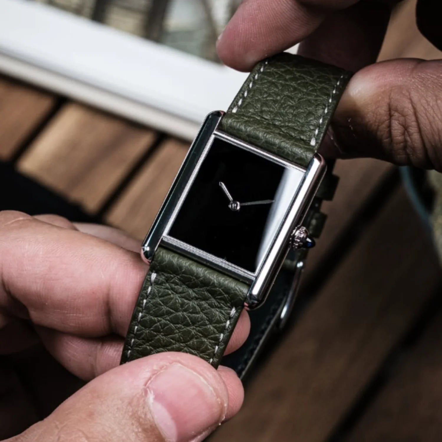 A person holding the silver CILOA square watch, showing the polished 10mm stainless steel case depth and a green pebbled leather wristband