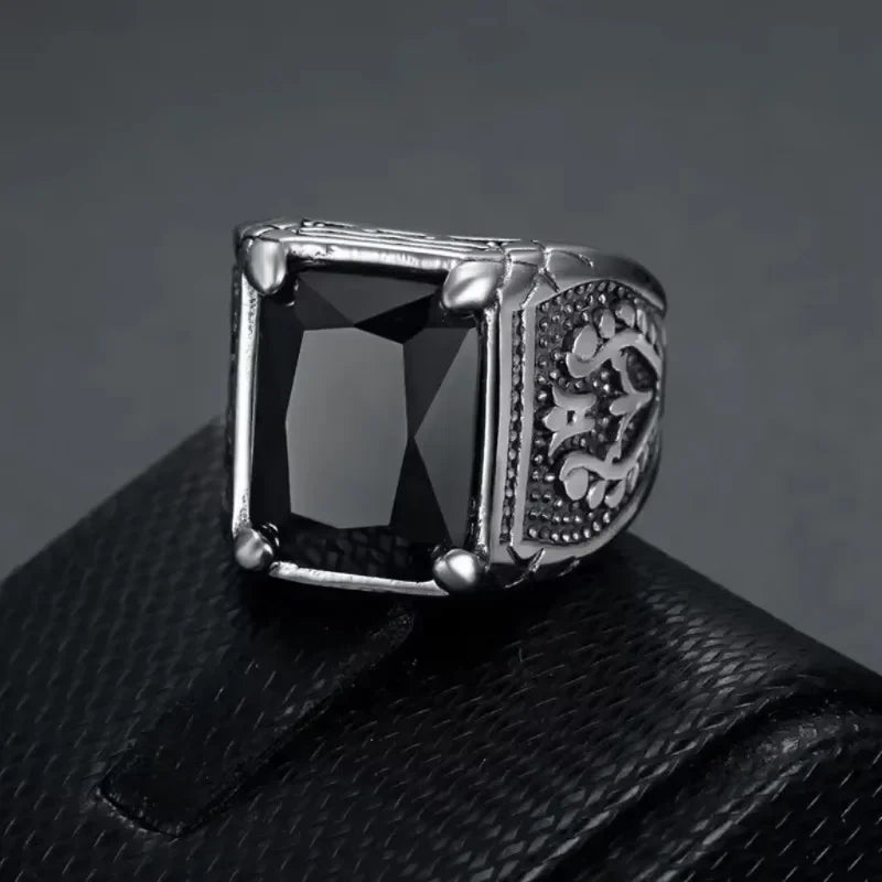 Engraved silver signet ring with a black rectangular stone resting on a dark leather display.