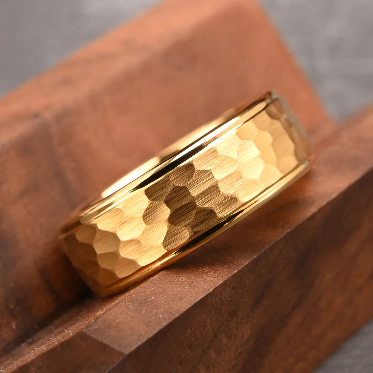 A single gold-plated hammered tungsten wedding band resting elegantly on a warm brown rustic wooden block