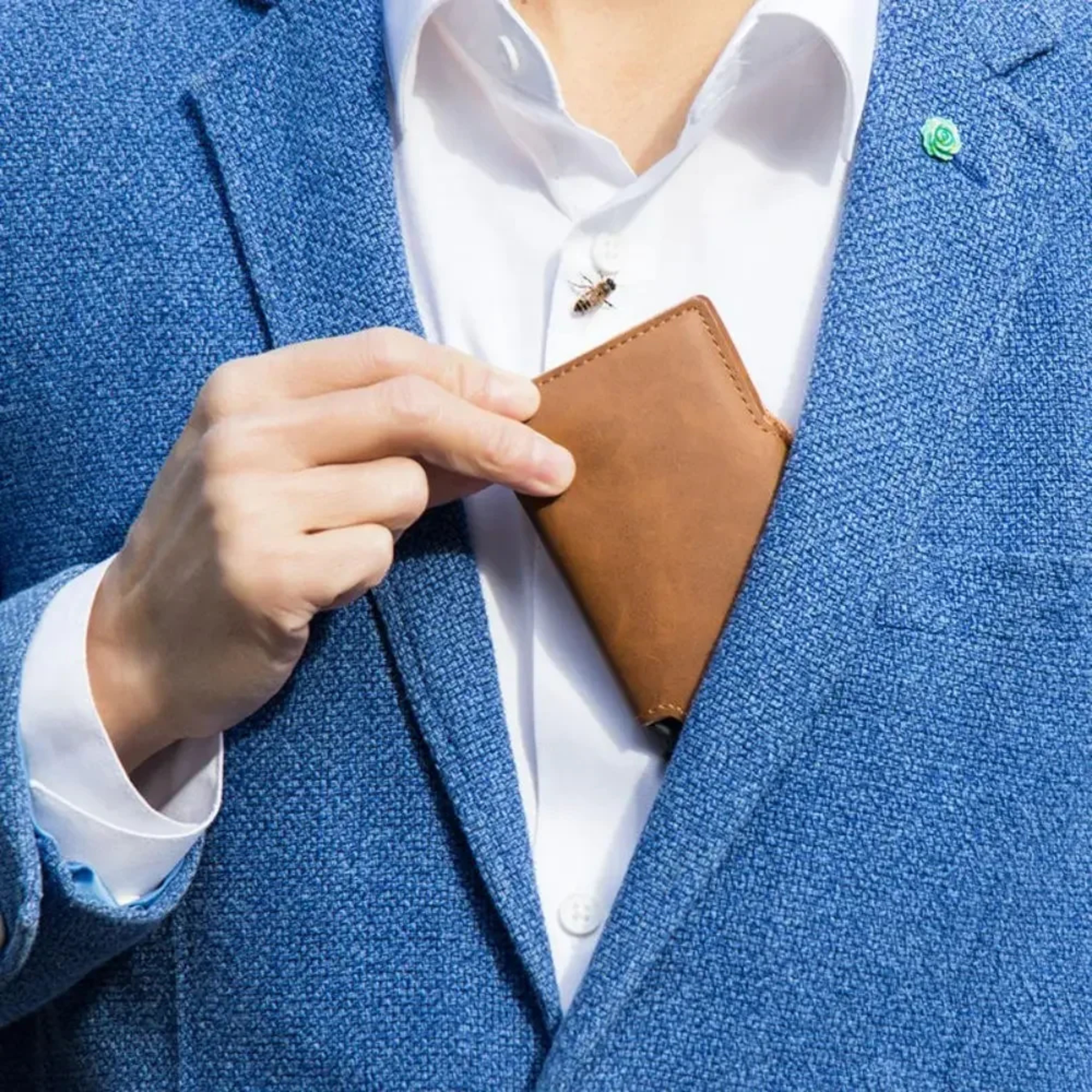 Close-up of a gentleman dressed in a sharp blue tailored blazer sliding the ultra-thin tan leather pop-up wallet seamlessly into his interior breast pocket