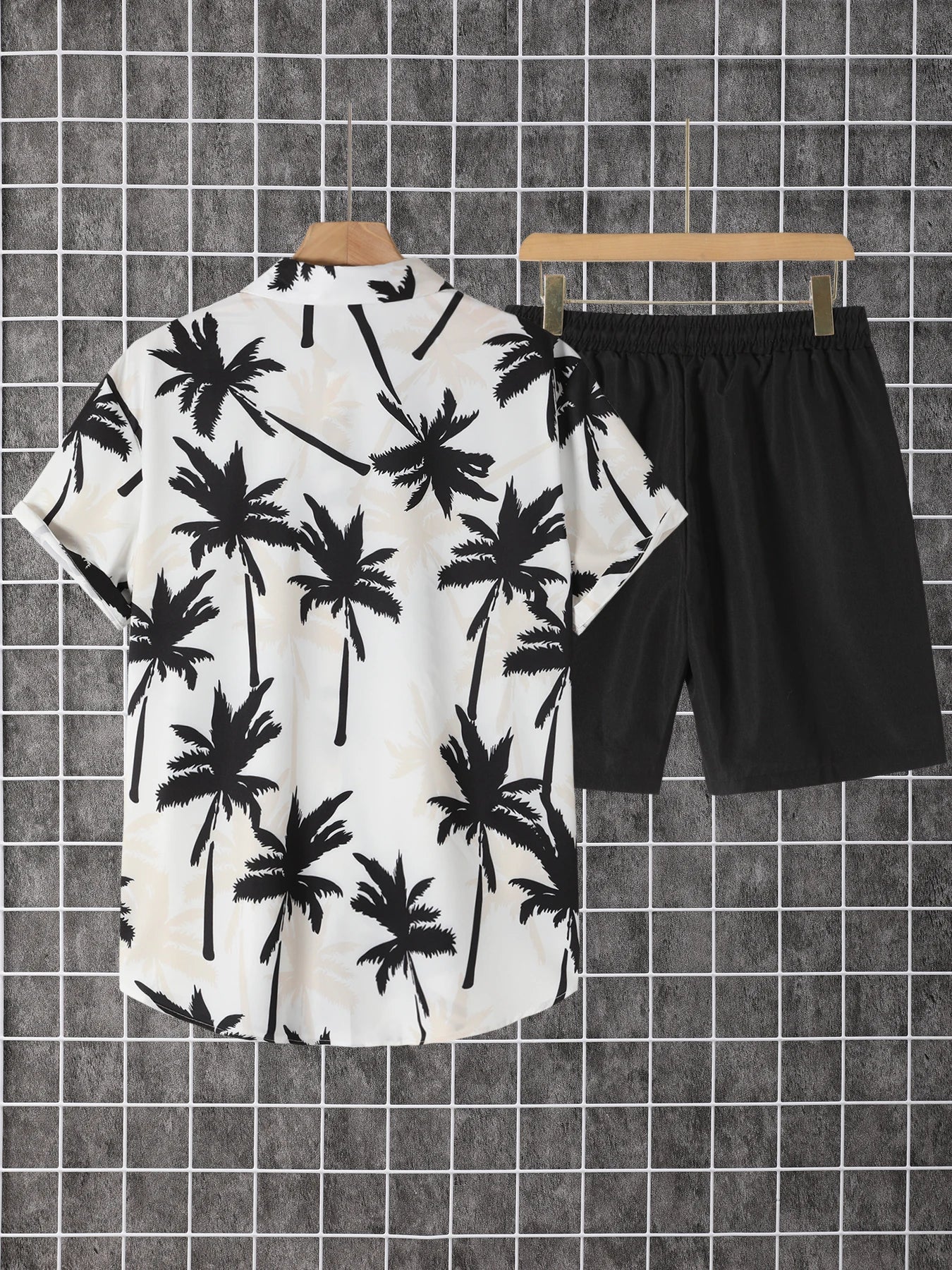 E-commerce product catalog presentation of the black palm tree printed button-down shirt and black drawstring shorts against a grey tiled background