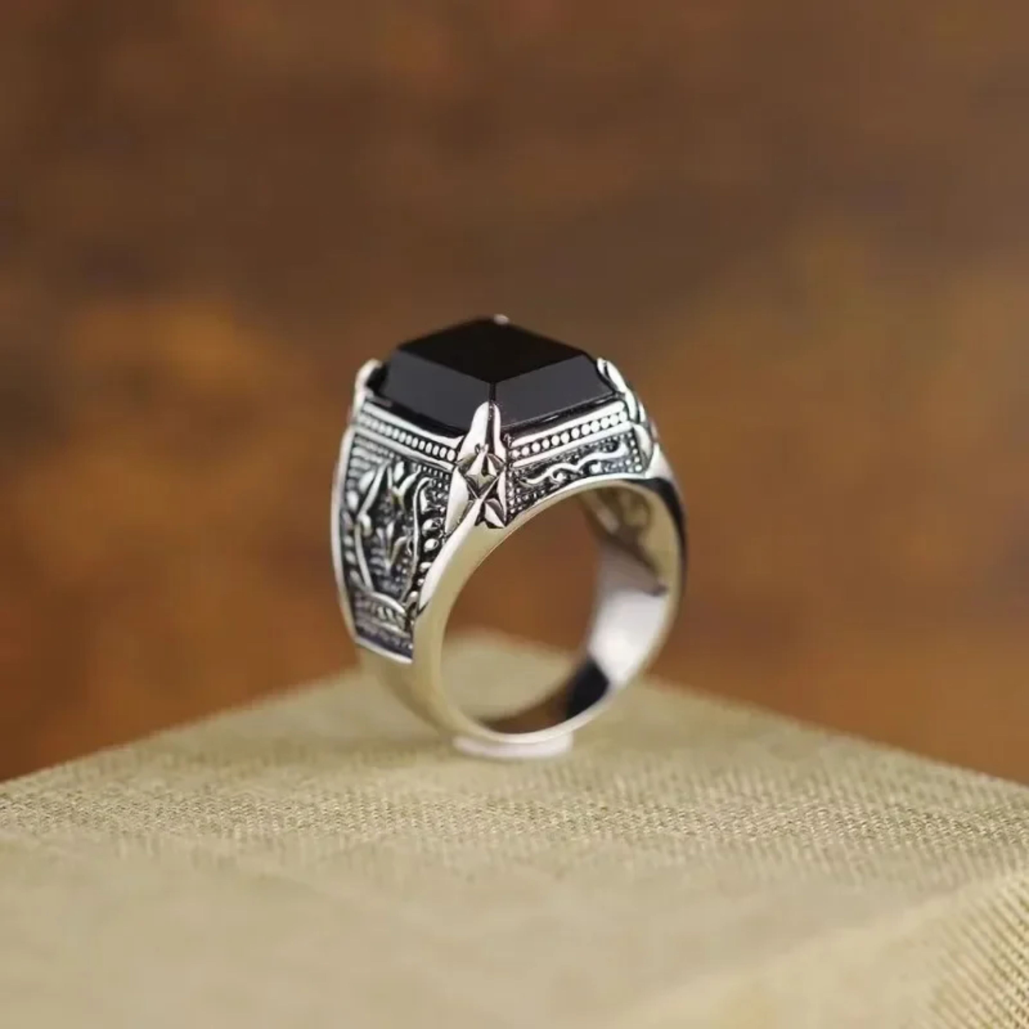 Men's chunky silver signet ring with a black rectangular stone resting on a beige display block.