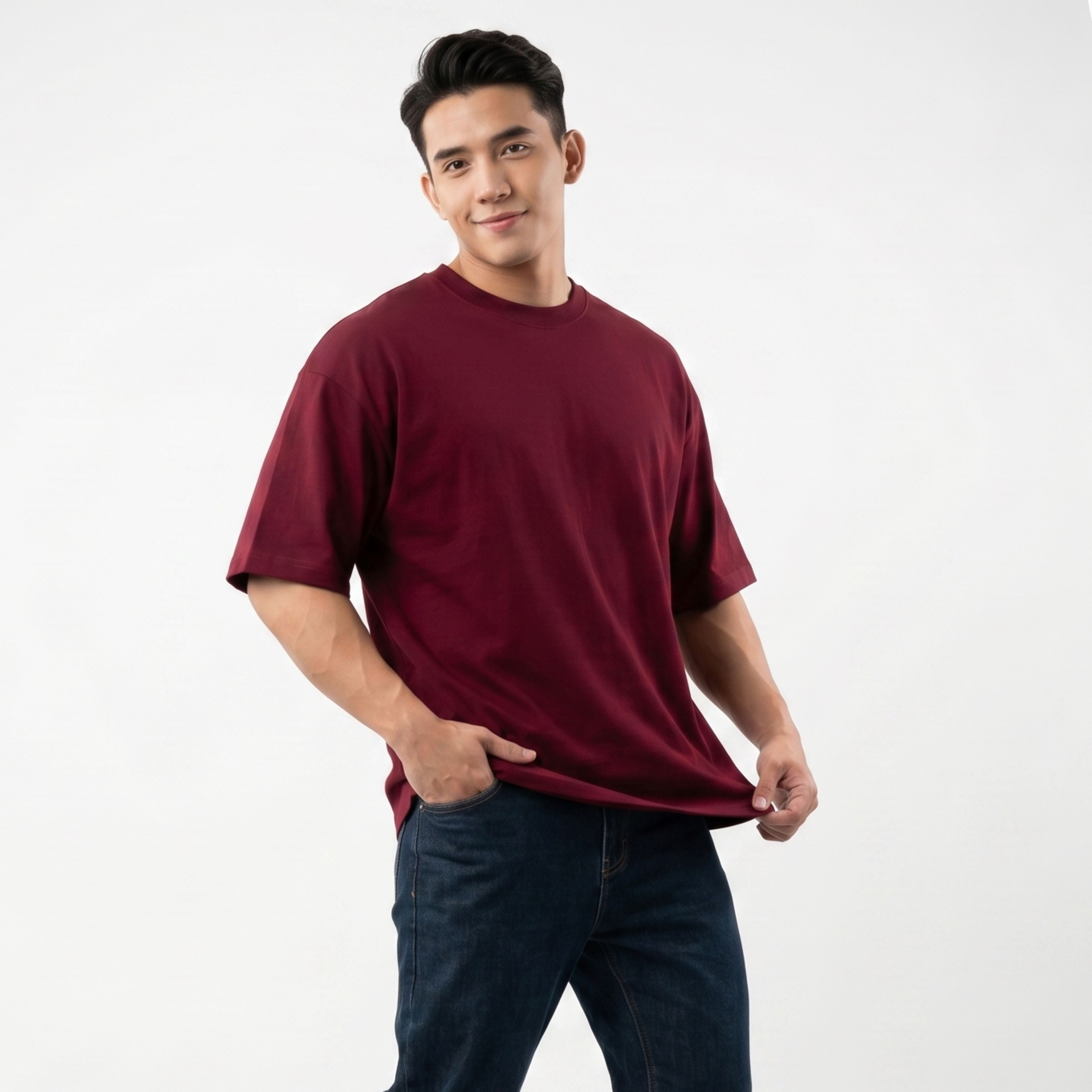A male model wearing the oversized 425g heavy knit cotton t-shirt in burgundy wine red, paired with dark denim jeans