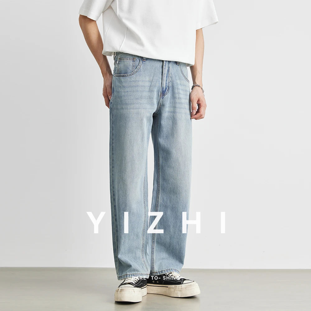 Three-quarter front view of a male model wearing light wash loose wide-leg denim pants paired with black canvas sneakers