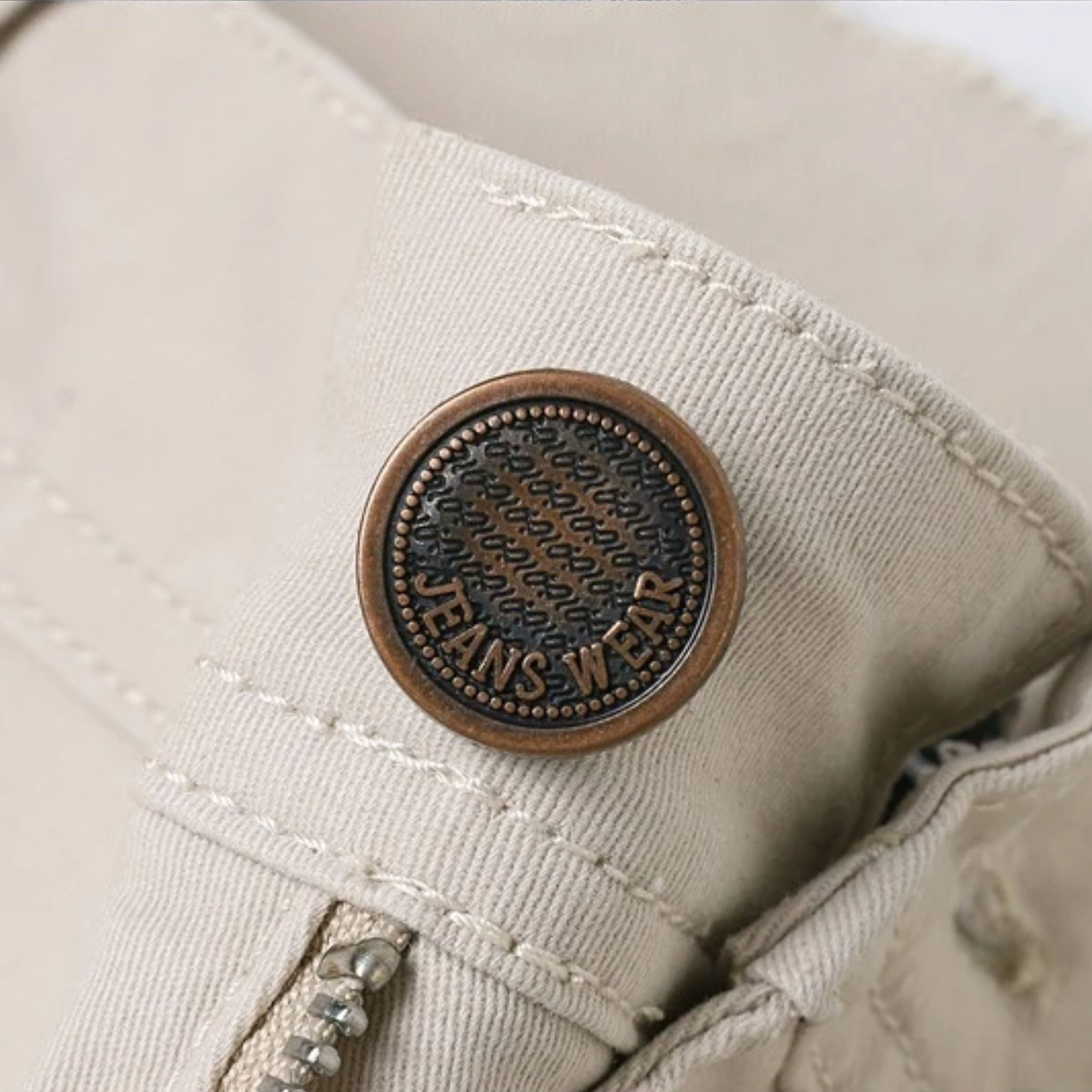 Macro close-up shot of the antique bronze top waist button engraved with specialized denim branding text, secured tightly on the waistband fabric