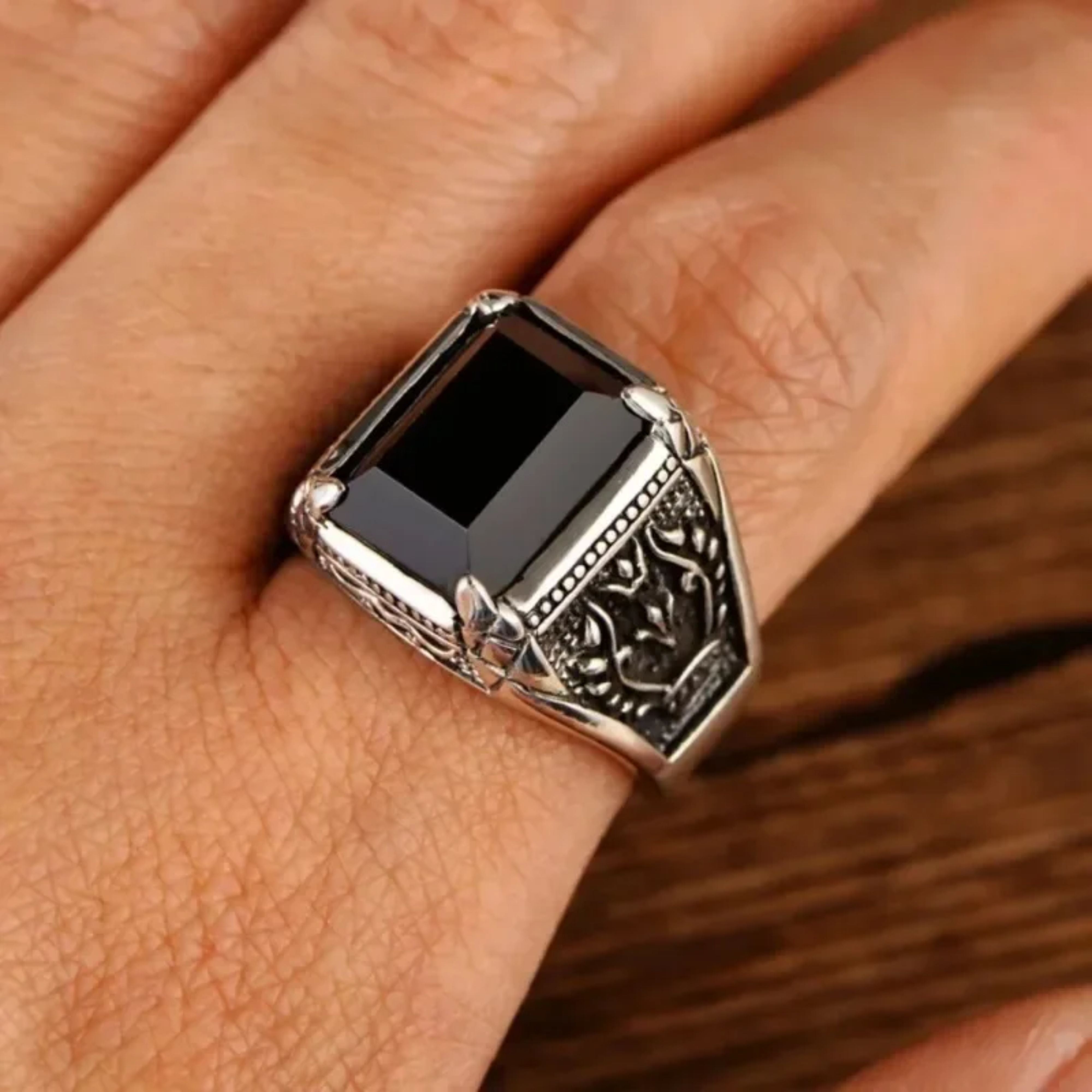 Men's vintage silver signet ring with a black gemstone being worn on a finger.