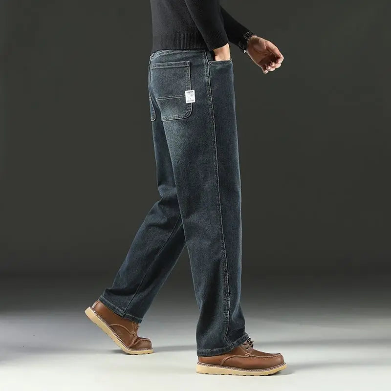 Side view of a model walking in dark blue loose fit stretch jeans, highlighting the clean tatting weave structure over heritage leather boots