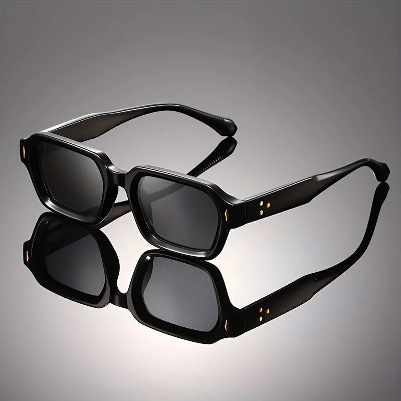 Retro chunky rectangular sunglasses in a solid black acetate frame reflecting on a dark studio surface.