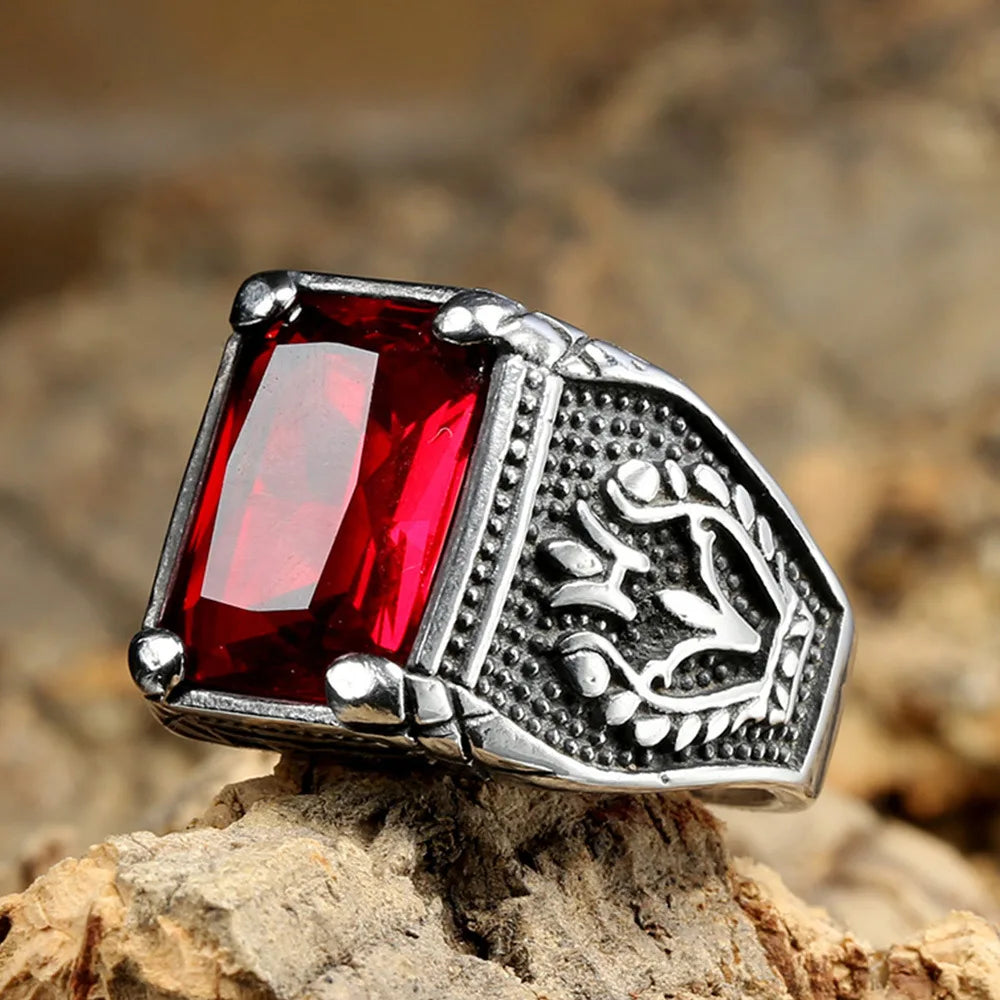 Retro silver signet ring with a large red gemstone resting on rustic textured wood bark.