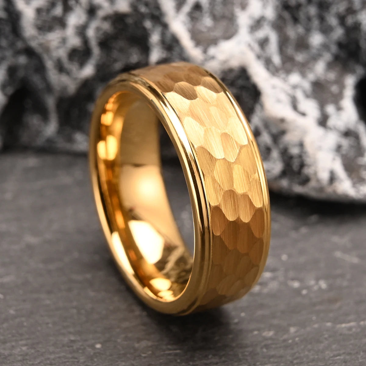 Angled shot of the heavy-duty 24k gold-plated hammered tungsten fashion ring set against a coarse dark rock environment