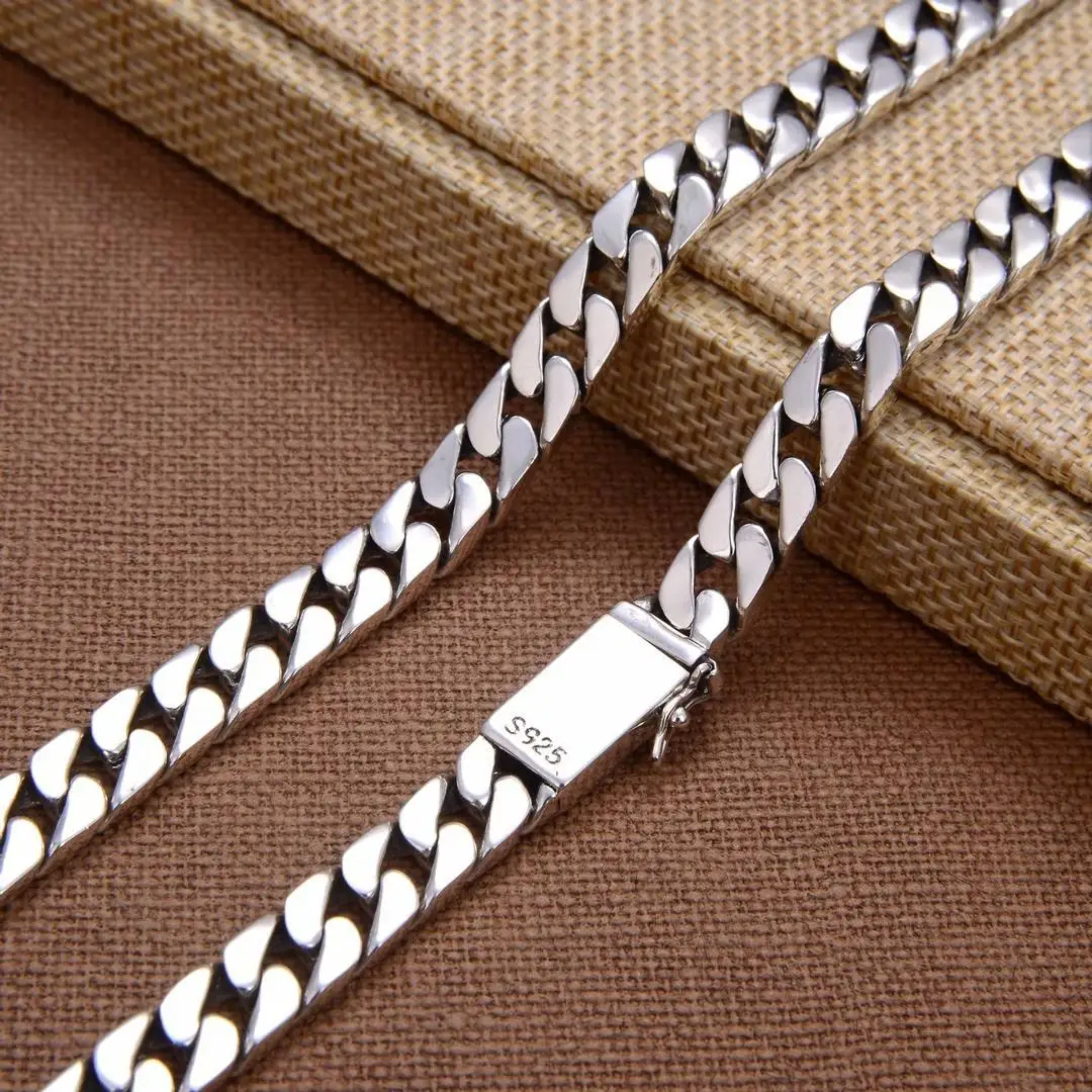 Close-up of a silver Cuban link chain and its secure box clasp resting on a brown surface.