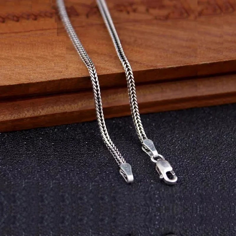 Close-up of the lobster clasp and end links of a silver foxtail chain resting near a wooden surface.