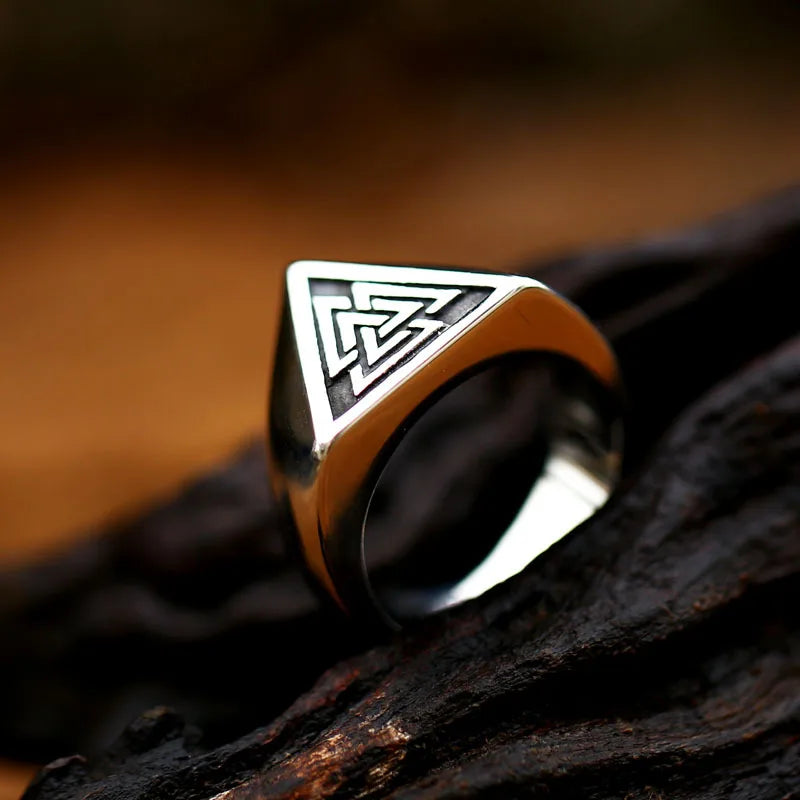 Silver ring featuring the Norse interlocking triangles symbol, also known as the Valknut, placed on dark bark.