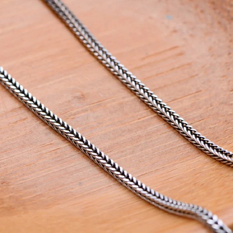Macro shot highlighting the intricate woven texture of a silver foxtail chain on a warm wooden background.