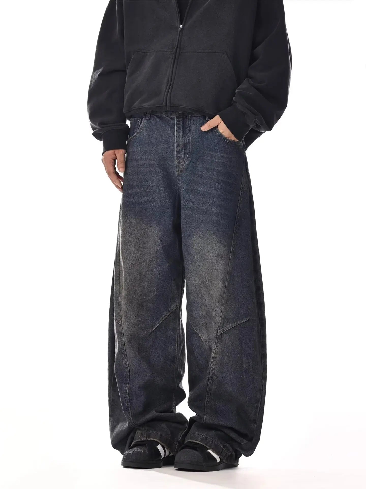 Oversized fit profile of a model wearing dark indigo blue faded denim trousers with stacked sneaker pools