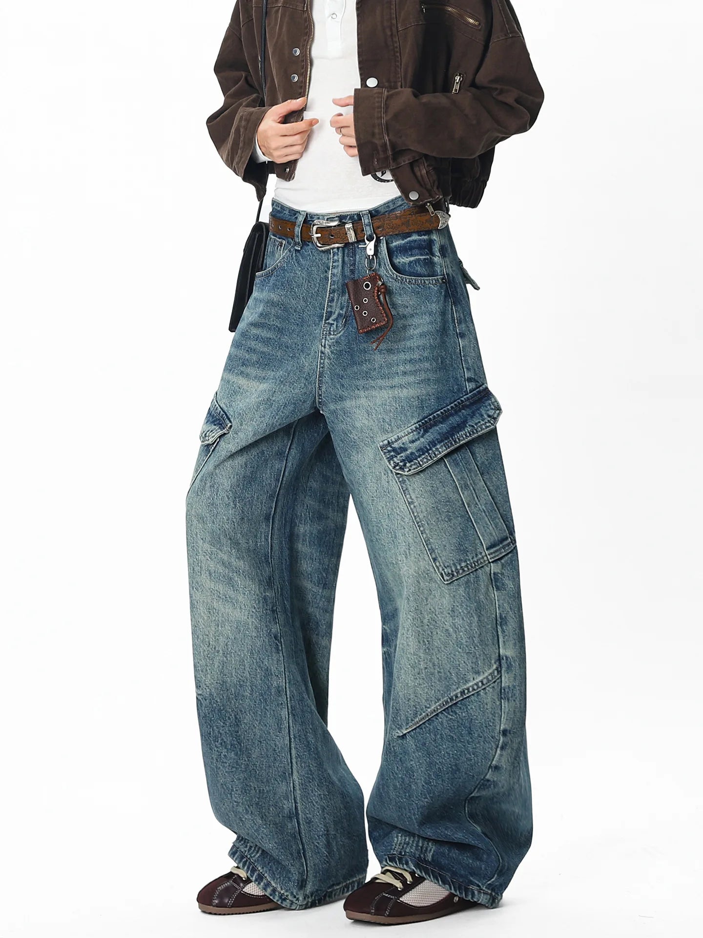 Full front view of a model wearing high-street blue baggy cargo jeans with large utility side pockets and leather belt accents