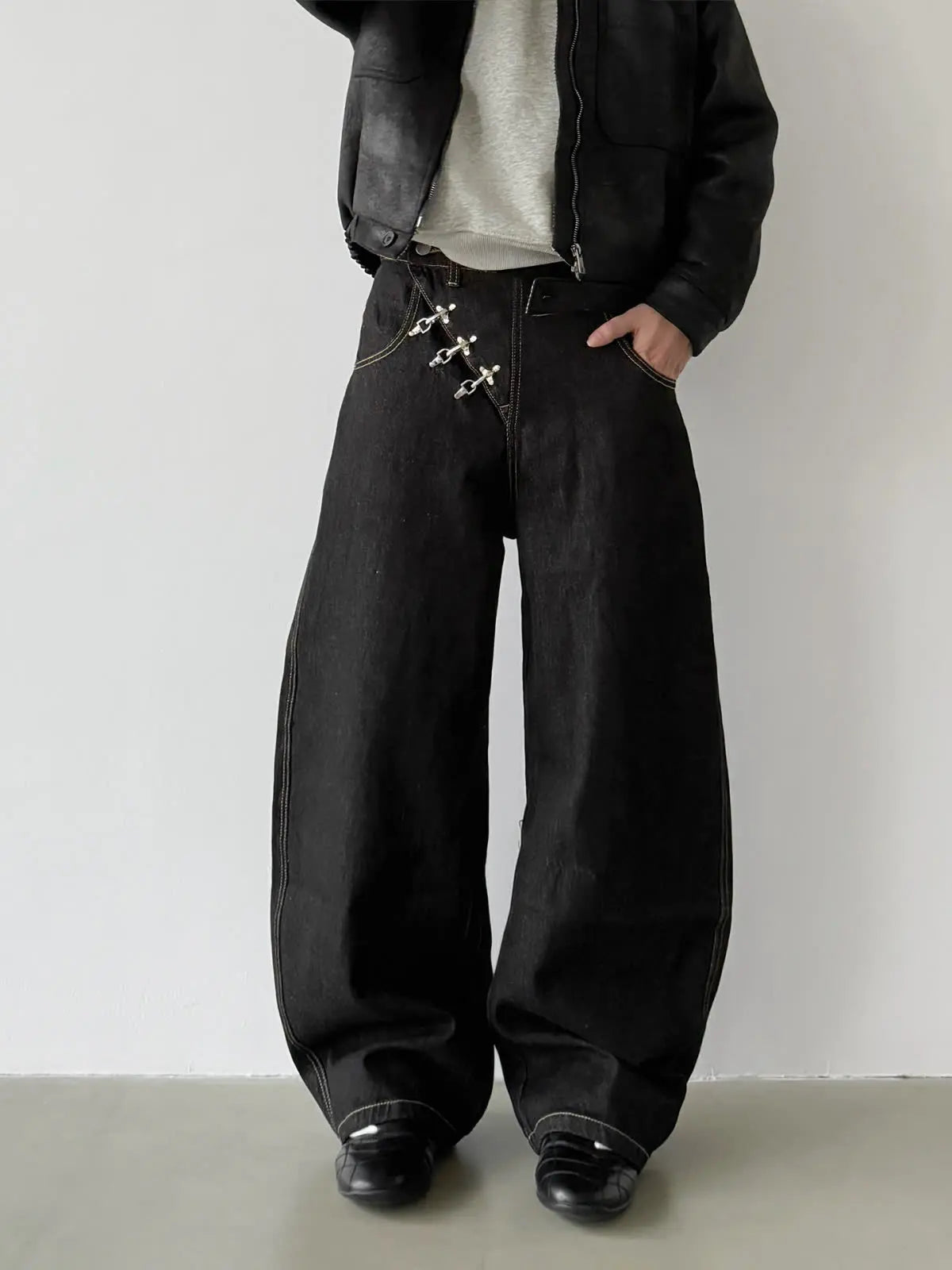 Minimalist front view of a model wearing washed black rigid denim baggy pants with signature metallic belt-loop pins