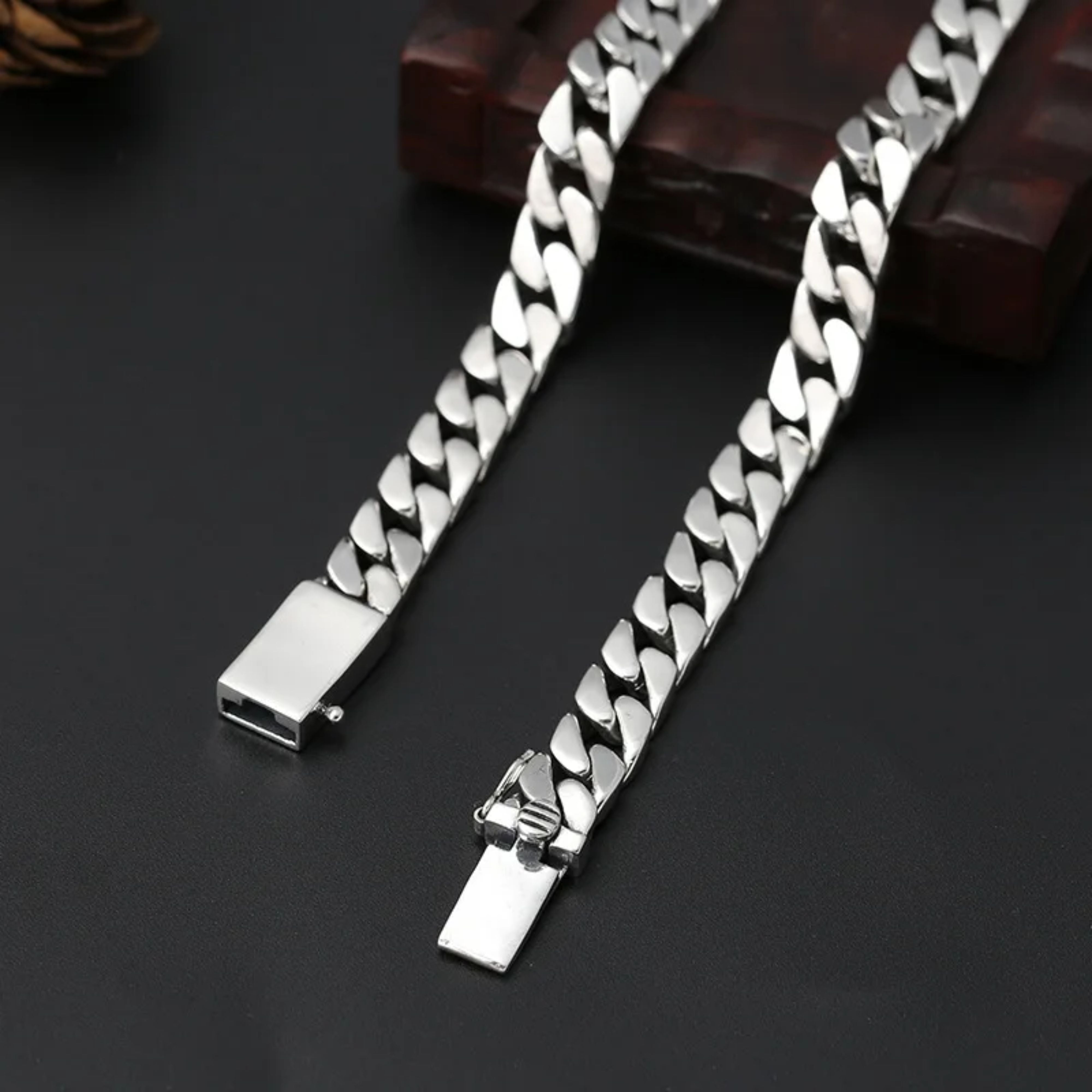 Thick silver Cuban chain necklace shown with its box clasp unclasped, draped over a dark background.